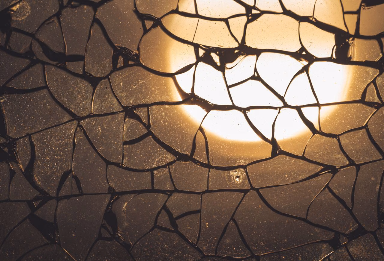 Bruchmuster durch Temperaturspannungen Zersprungenes Glas mit feinem Rissnetz und starkem Lichteinfall, wie es bei thermisch bedingten Spannungen in einer Glasscheibe auftreten kann.