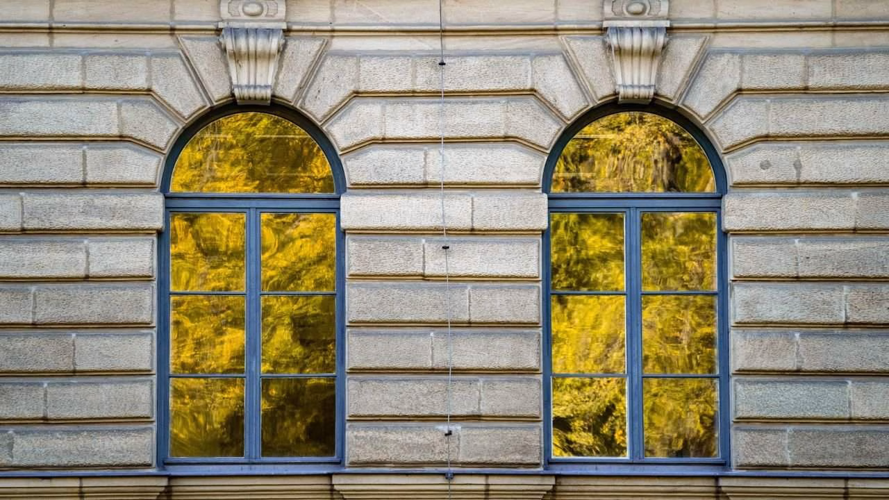 Reflektierende Fensterflächen zeigen anschaulich, wie Spiegelfolie den Blick von außen erschweren kann. Fensterfront mit starker Spiegelung von Bäumen, die die Wirkung von Spiegelfolie bei Tageslicht zeigt