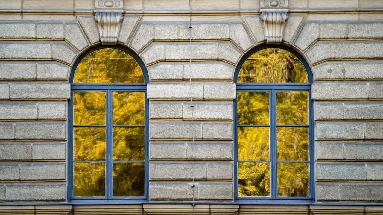 Reflektierende Fensterflächen zeigen anschaulich, wie Spiegelfolie den Blick von außen erschweren kann. Fensterfront mit starker Spiegelung von Bäumen, die die Wirkung von Spiegelfolie bei Tageslicht zeigt
