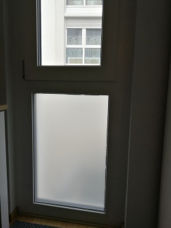 Eine weiß matte, selbsthaftende Sichtschutzfolie auf einem feststehenden Fenster angebracht