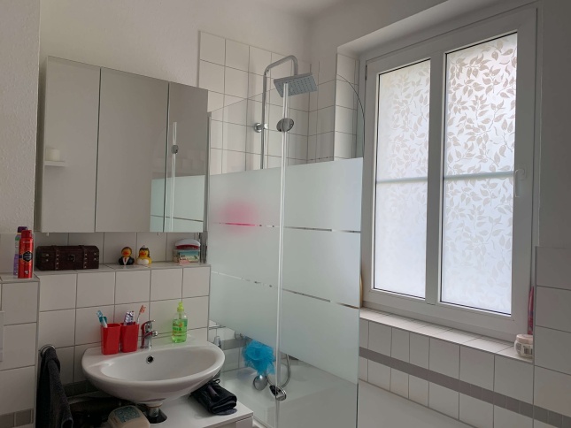 Sichtschutzfolie mit weißen Blättern auf einem Badezimmerfenster geklebt